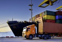 Truck transportation carrying forty-foot container leaving port terminal with ship and quay crane on the background