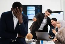 group of business people pointing and talking rumor spread behind stress colleague at workplace, diverse coporate employee gossip and bully black person while meeting in financial office.